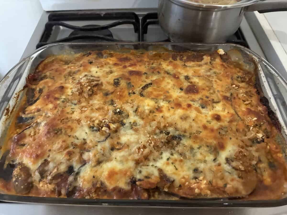 A baked casserole topped with melted, browned cheese sits on a stovetop next to a pot.