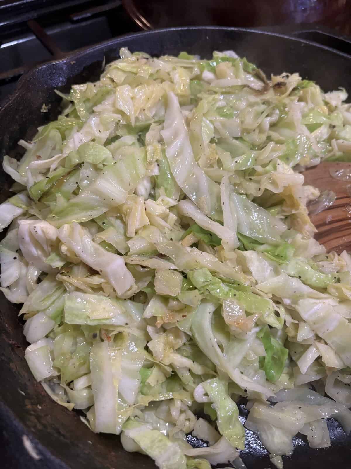 Chopped cabbage sautรฉing in a cast iron skillet, lightly seasoned and partially cooked.