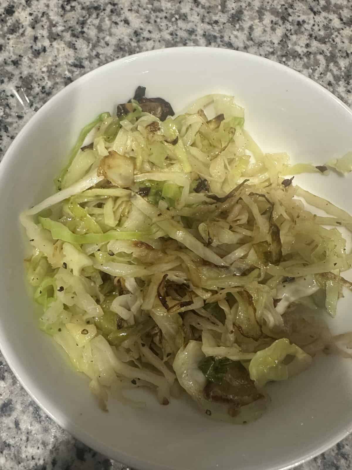 A white bowl filled with sautéed cabbage on a speckled countertop.