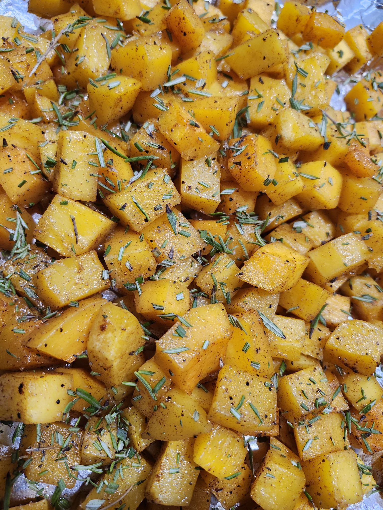 Cubed roasted yellow potatoes seasoned with herbs and black pepper on a foil-lined baking tray.