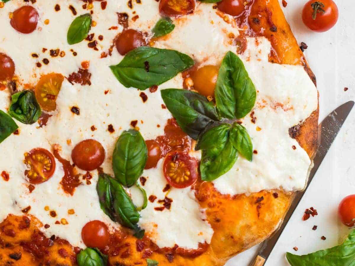 Burrata pizza on a white counter with fresh basil