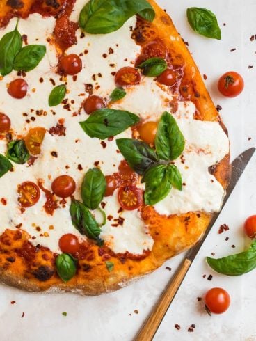 Burrata pizza on a white counter with fresh basil