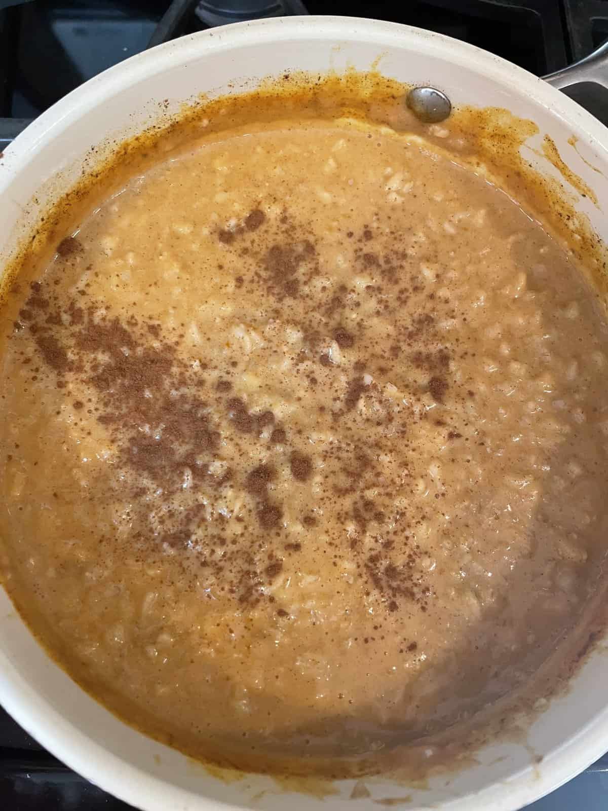 A pot of creamy rice pudding with cinnamon sprinkled on top, cooking on a stovetop.