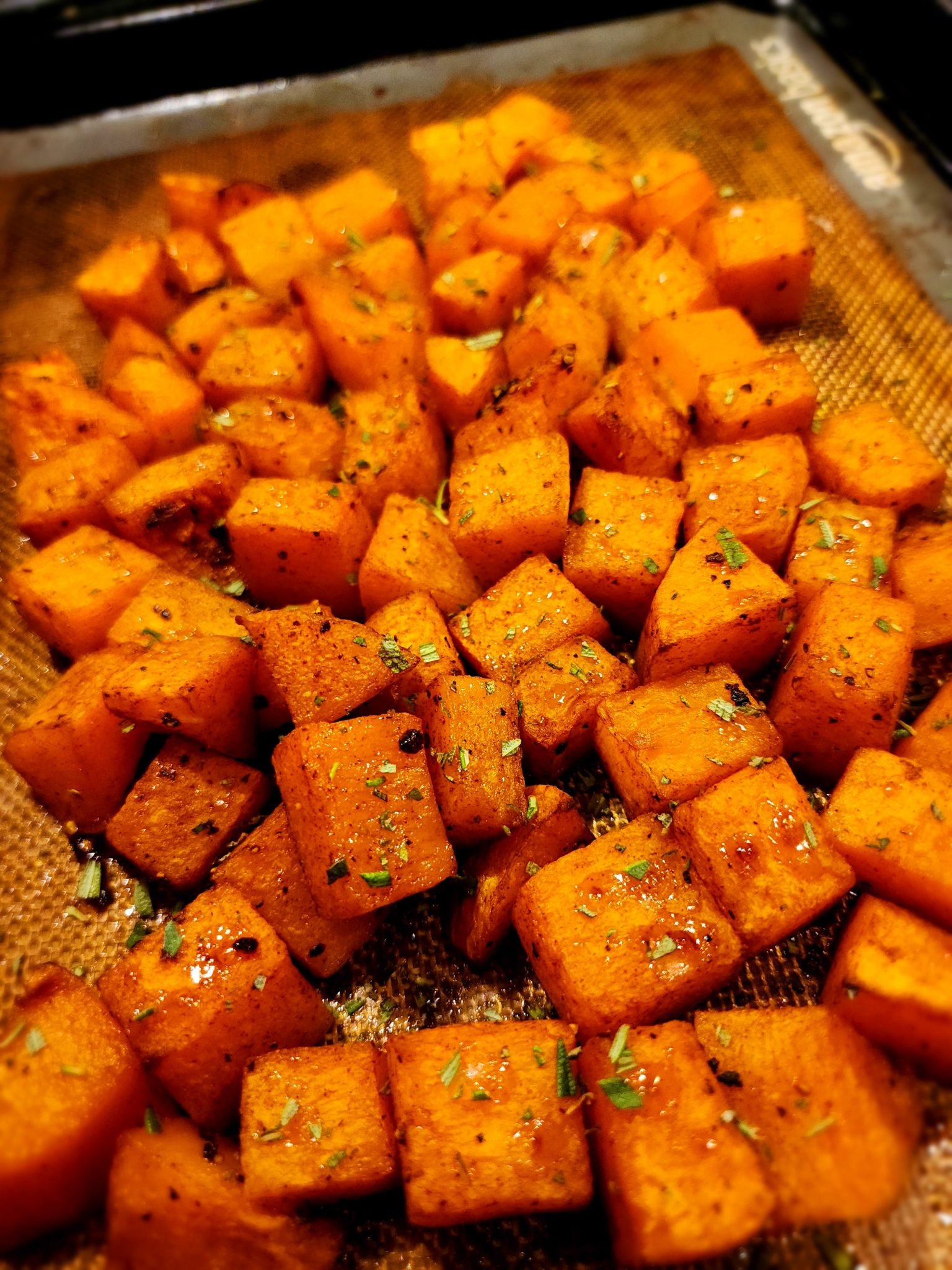 Cubed roasted butternut squash seasoned with herbs and spices on a baking mat.