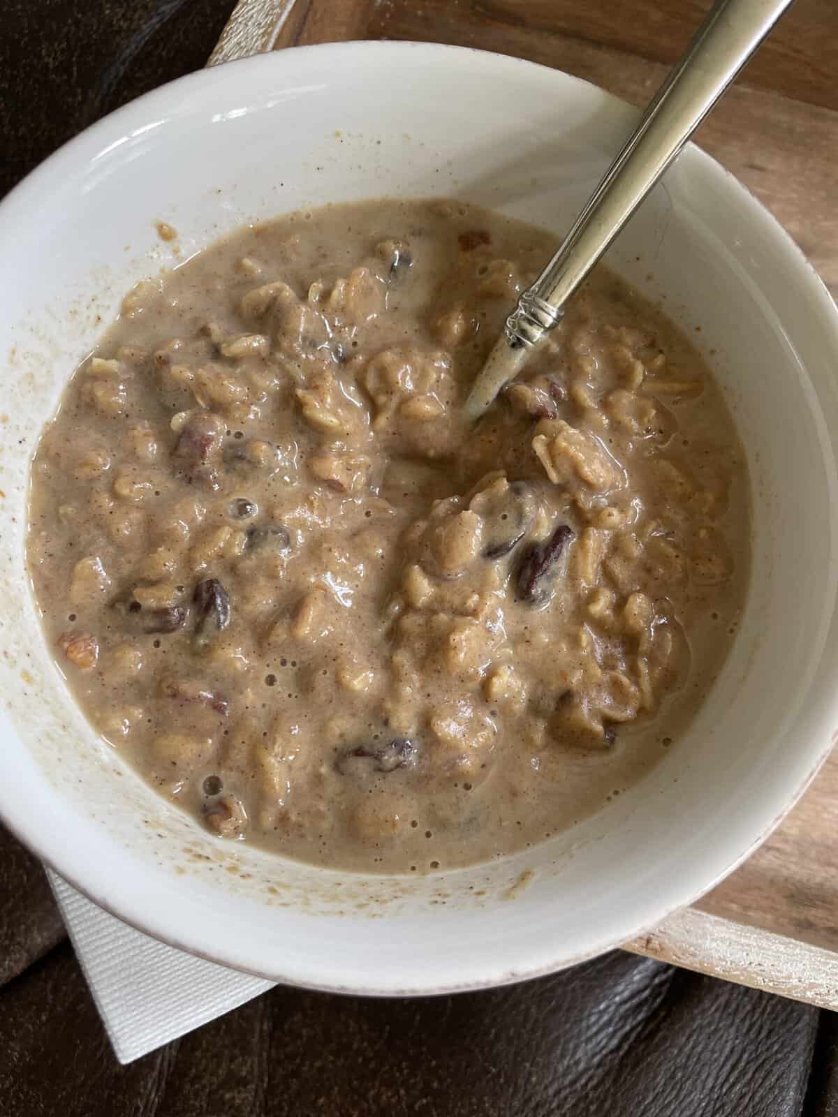 A bowl of oatmeal with raisins and nuts, mixed with milk, and a spoon inside.