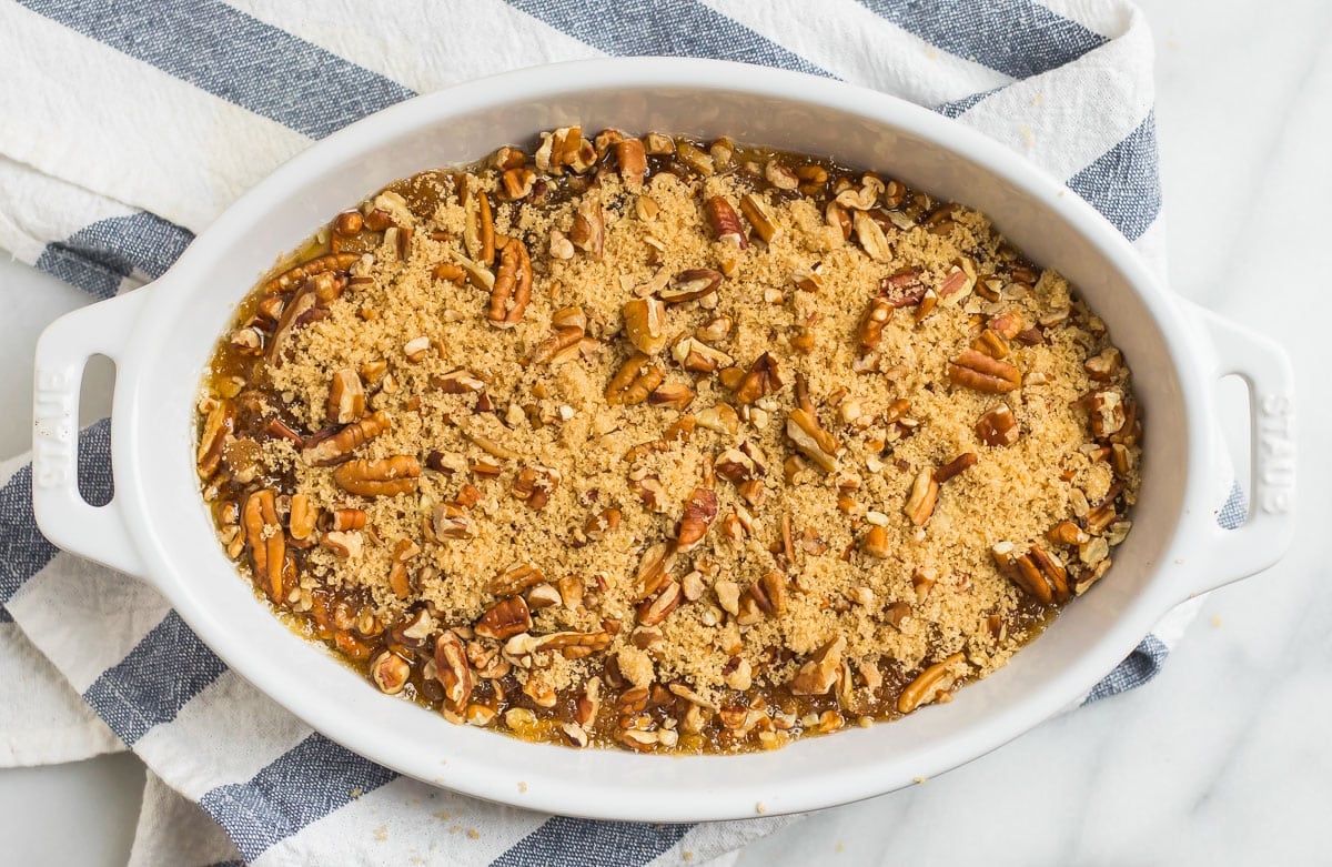 Oval baking dish with pecan-topped casserole on a striped towel, viewed from above.