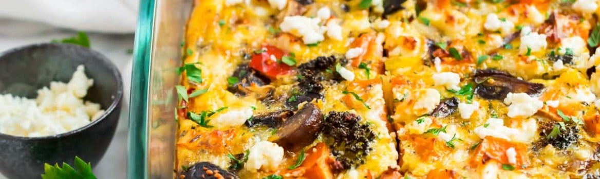 A glass baking dish with sliced vegetable egg casserole topped with herbs and cheese, on a cooling rack.