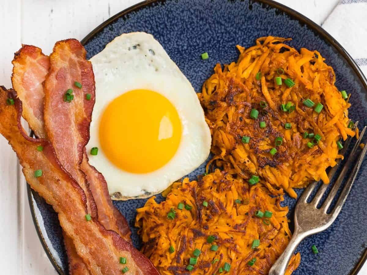 A blue plate with sweet potato hash browns, eggs, and bacon.