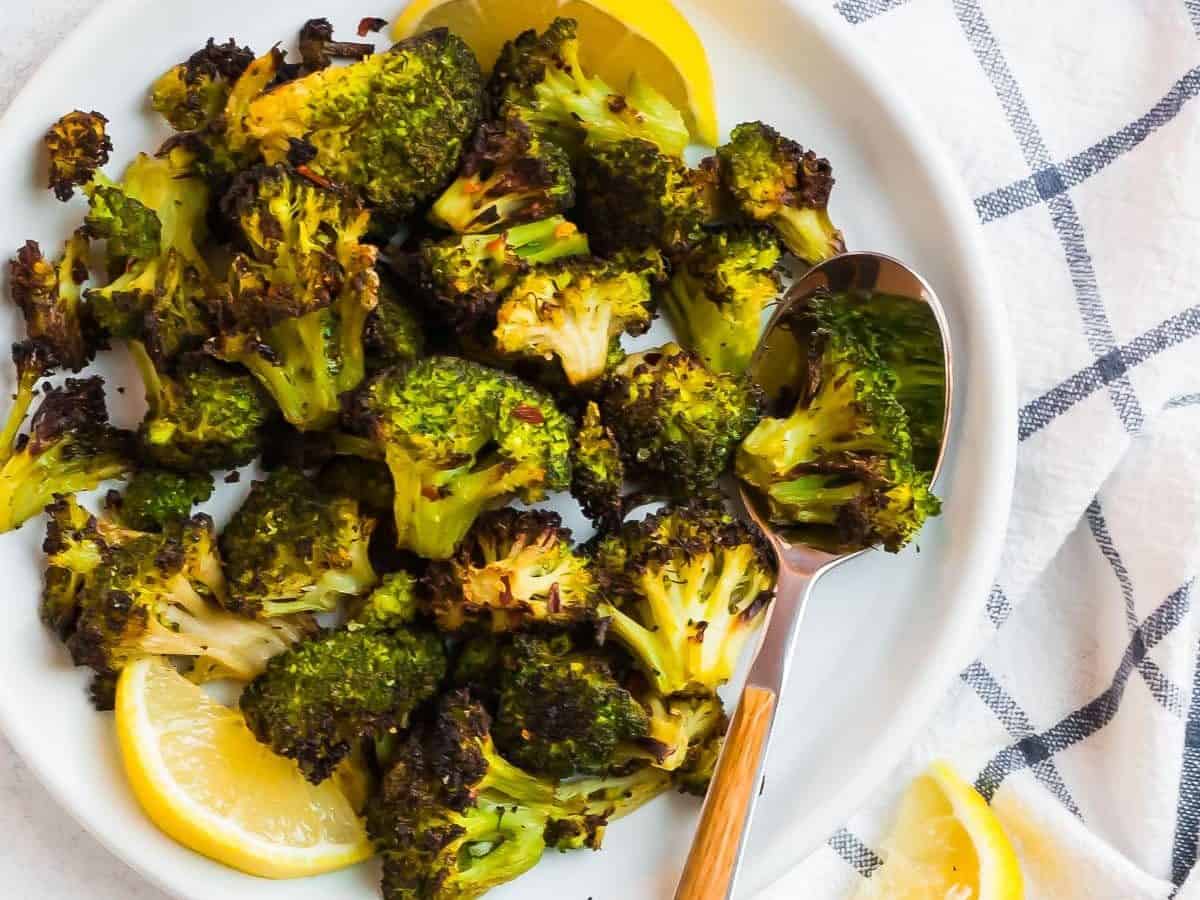 A white plate with roasted frozen broccoli and lemon slices