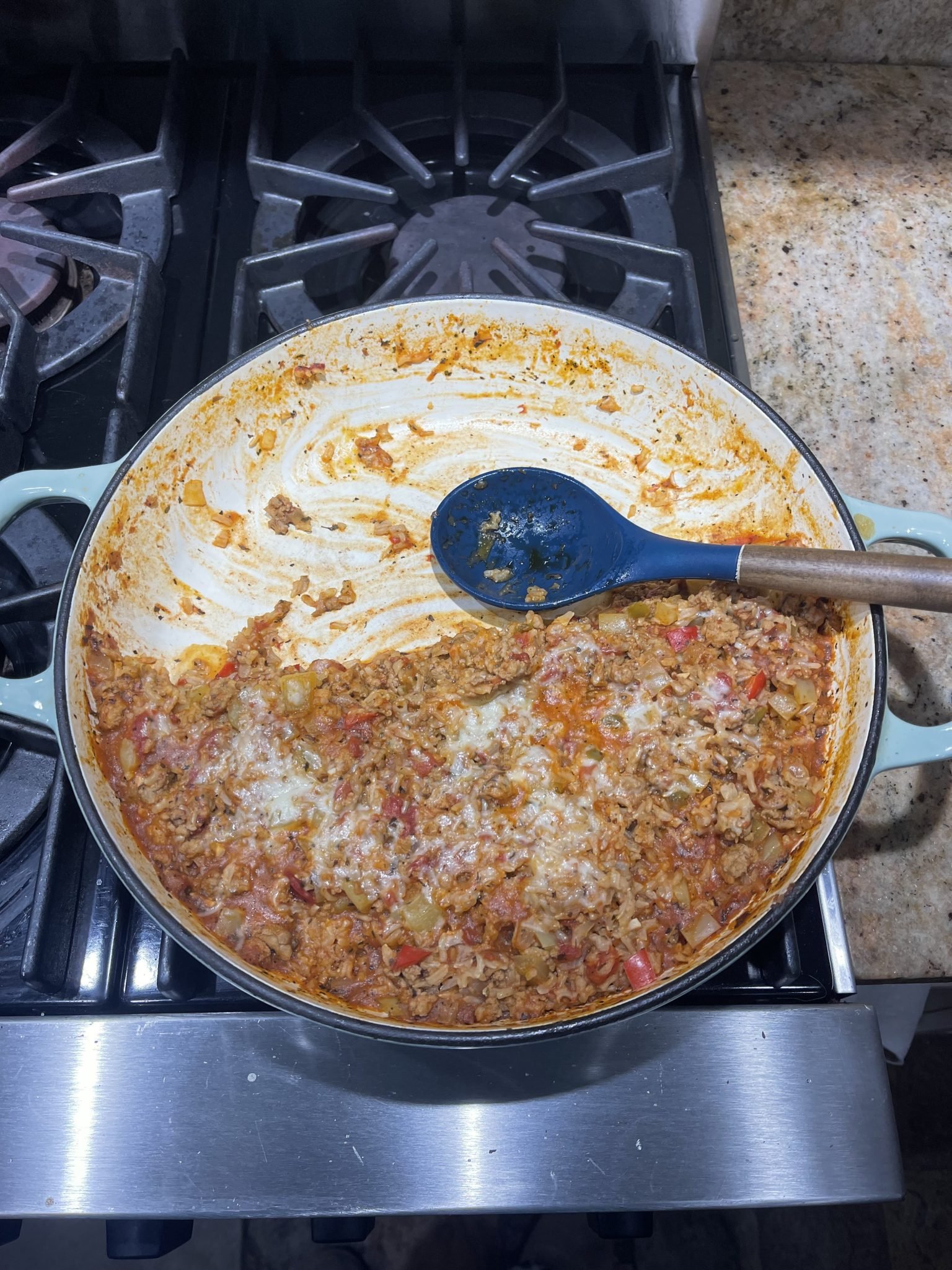 A pot of cooked ground meat with vegetables and sauce sits on a stovetop, with a wooden spoon resting inside.