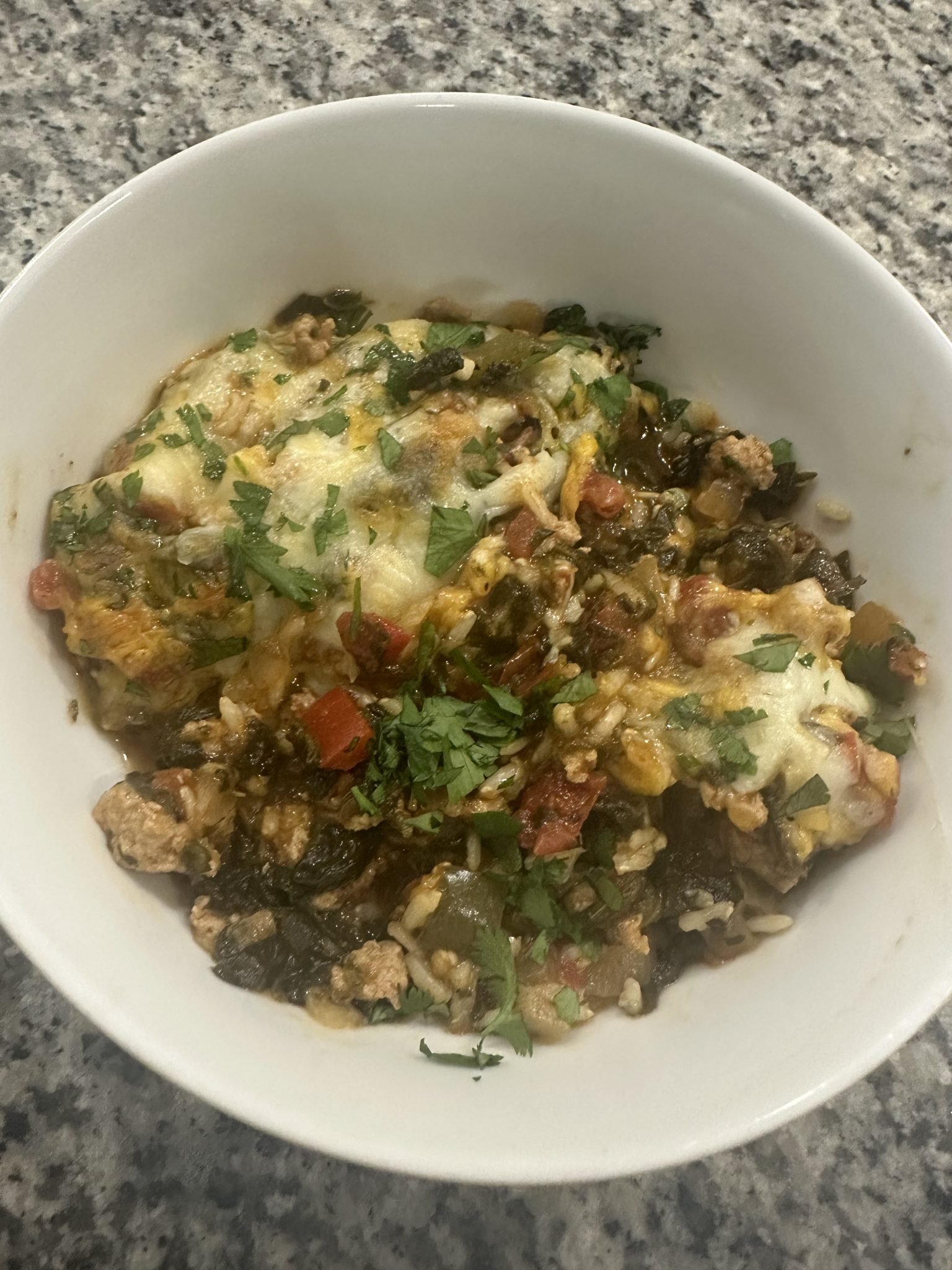 A white bowl filled with a cheesy, baked rice and vegetable casserole, garnished with chopped fresh herbs.