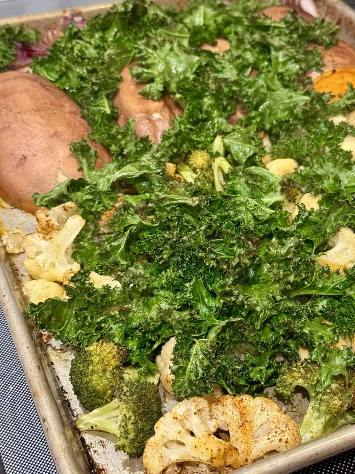 Roasted kale, cauliflower, broccoli, and sweet potatoes on a baking sheet, fresh out of the oven.