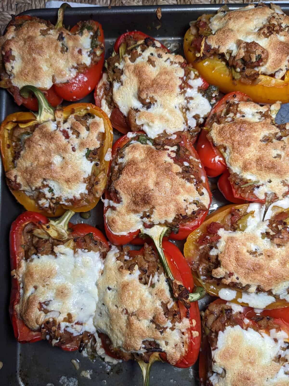Bell peppers stuffed with a meat and rice mixture, topped with browned melted cheese, arranged on a baking tray.