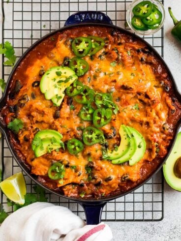 Cheesy skillet chicken enchiladas, served in a skillet and topped with avocado