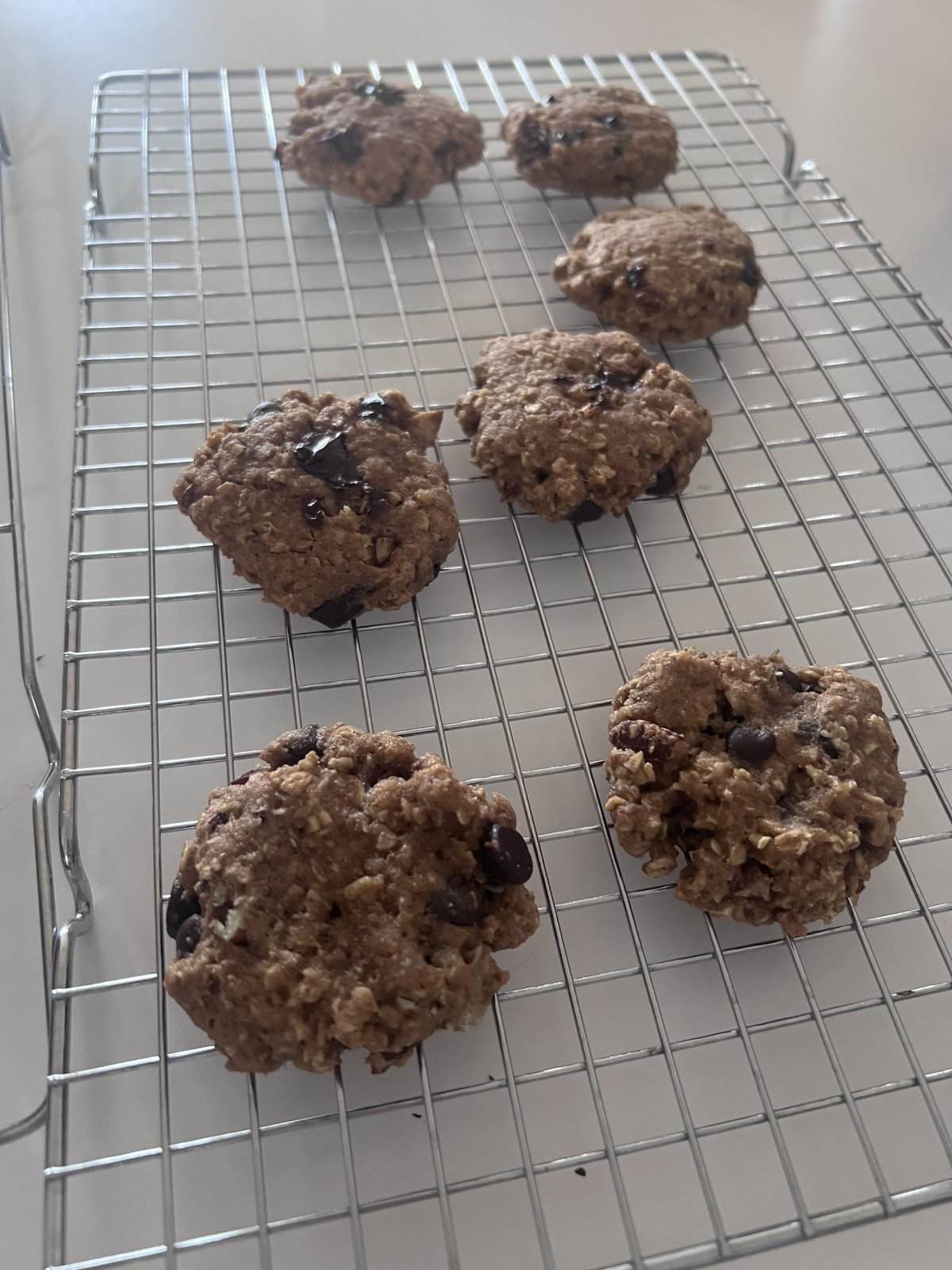 Six homemade chocolate chip cookies cooling on a metal wire rack on a white surface.