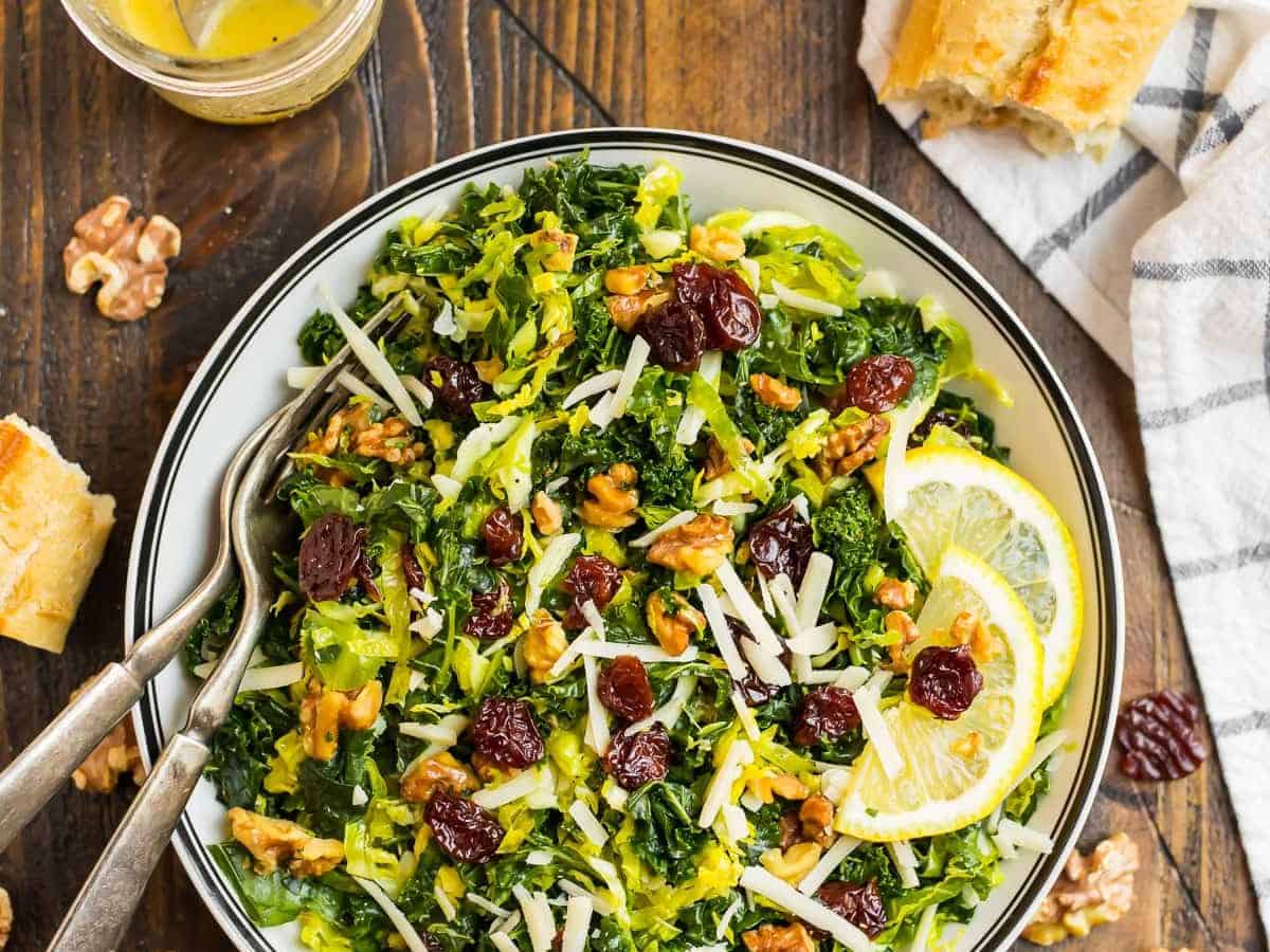 Kale and Brussel Sprout Salad with Maple Vinaigrette in a white salad bowl topped with walnuts