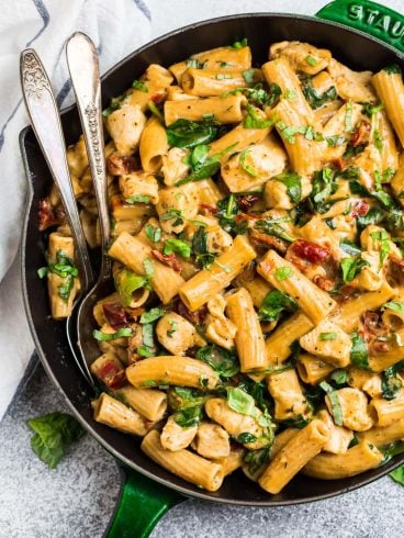 Cheesy Tuscan chicken macaroni and cheese in a skillet with two silver spoons