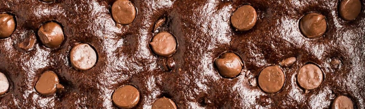Close-up of rich, glossy chocolate brownie batter topped with scattered chocolate chips.