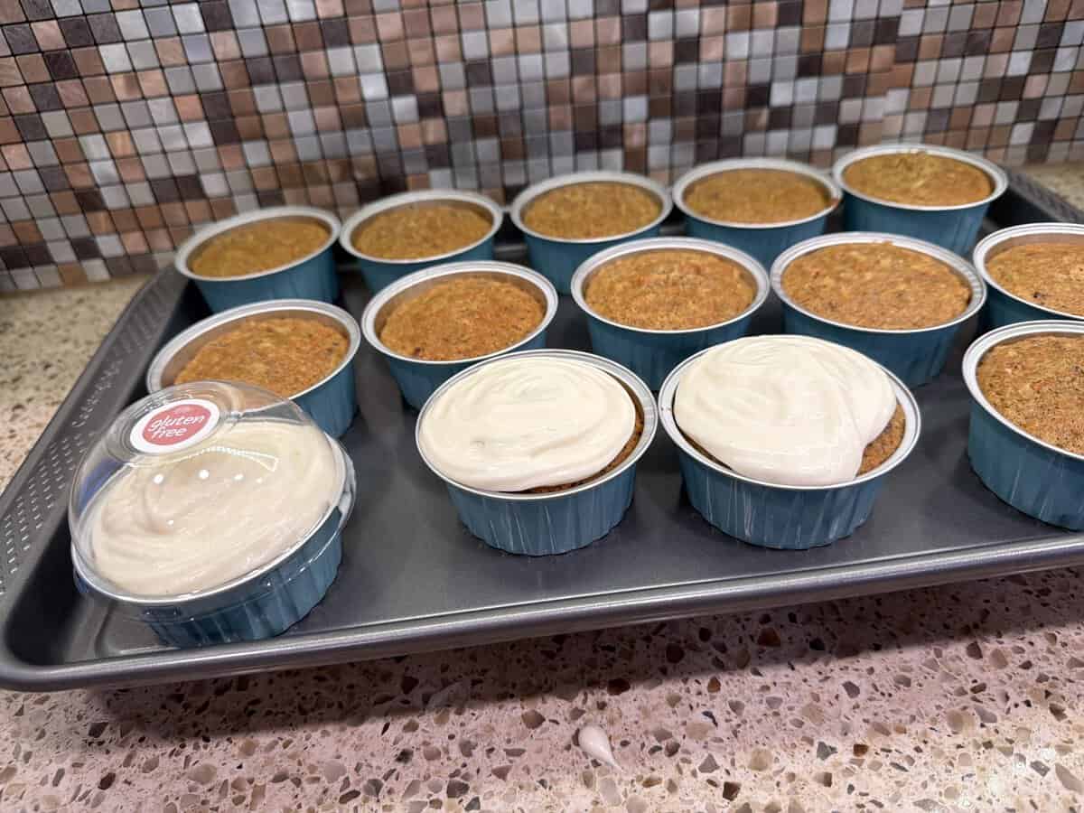 A tray of cupcakes, some frosted and some plain, in blue cups on a granite counter with a tile backsplash.