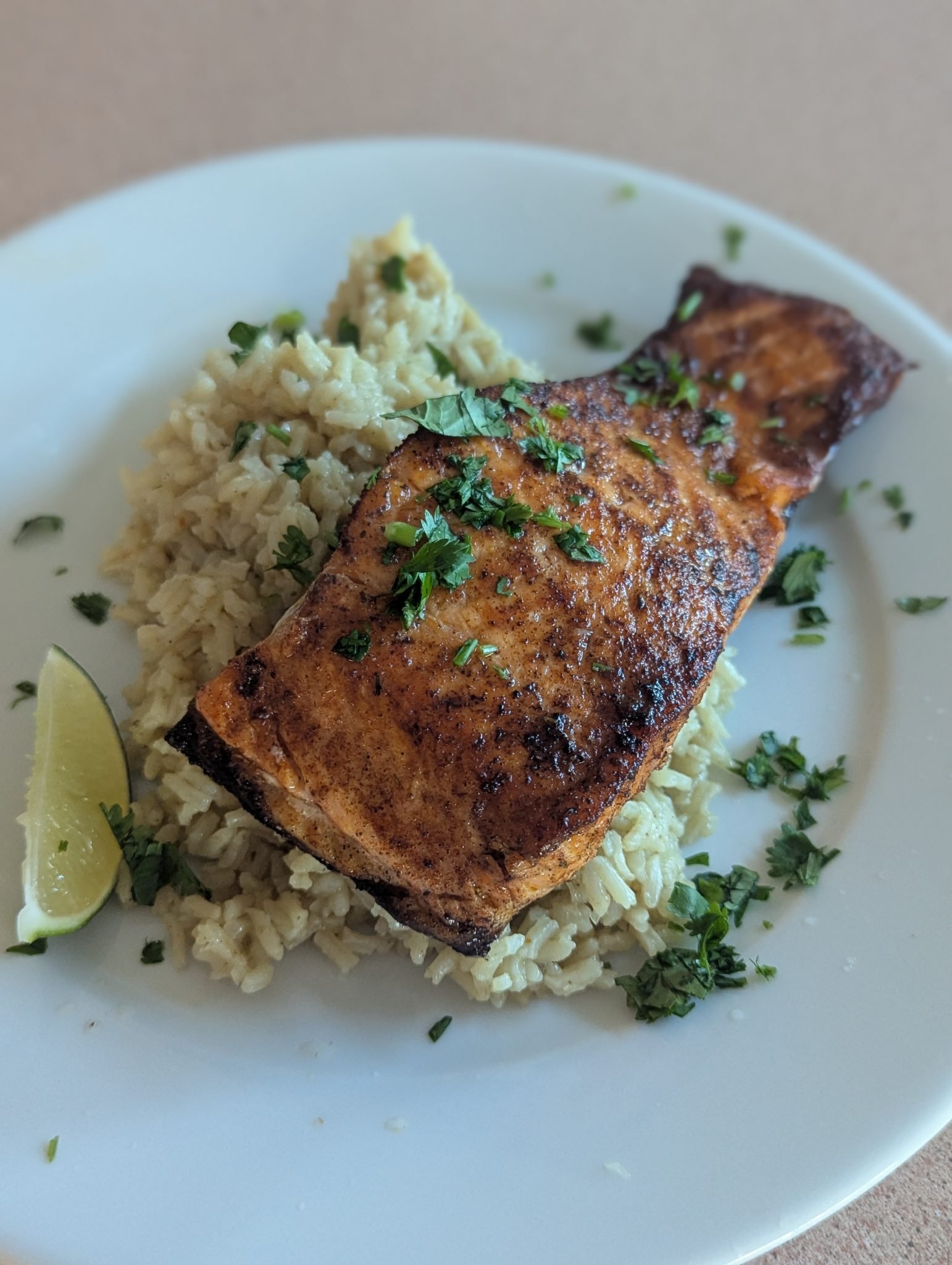 Grilled salmon fillet on a bed of rice, garnished with chopped herbs and a lime wedge on a white plate.