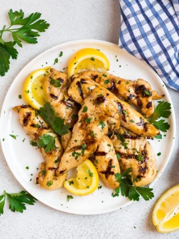 Delicious grilled chicken tenders on a white plate with lemon slices