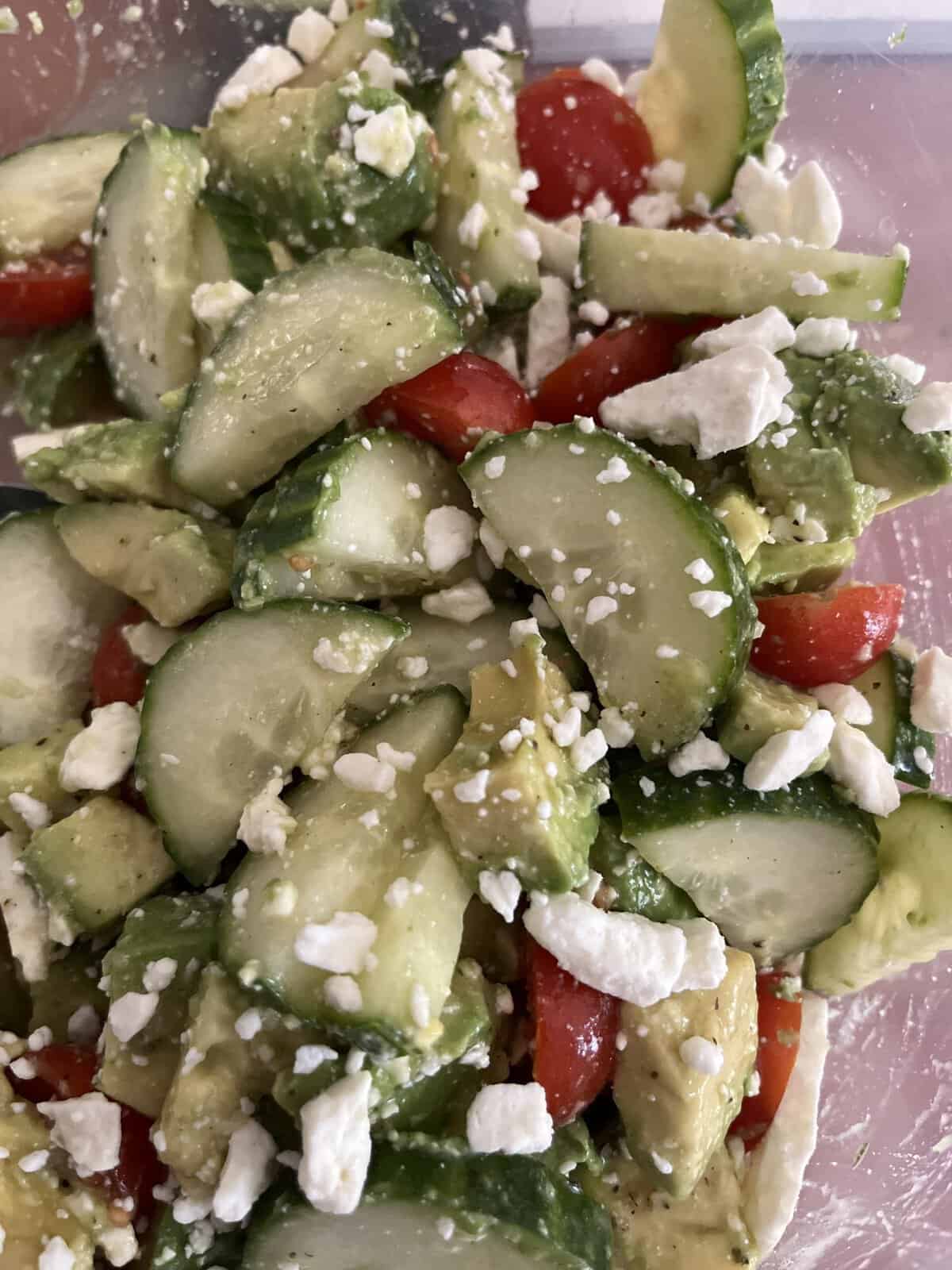 A close-up of a salad with cucumbers, cherry tomatoes, avocado, and crumbled feta cheese.