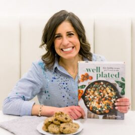 Erin Clarke holding the Well Plated Cookbook with a plate of chocolate chip cookies