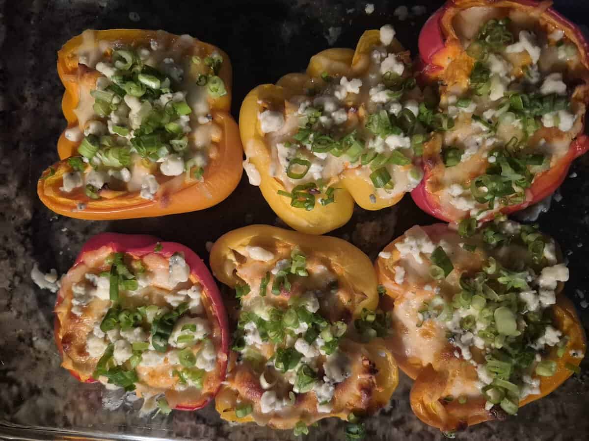 Six bell pepper halves, filled with cheese and topped with chopped green onions, arranged in a baking dish.