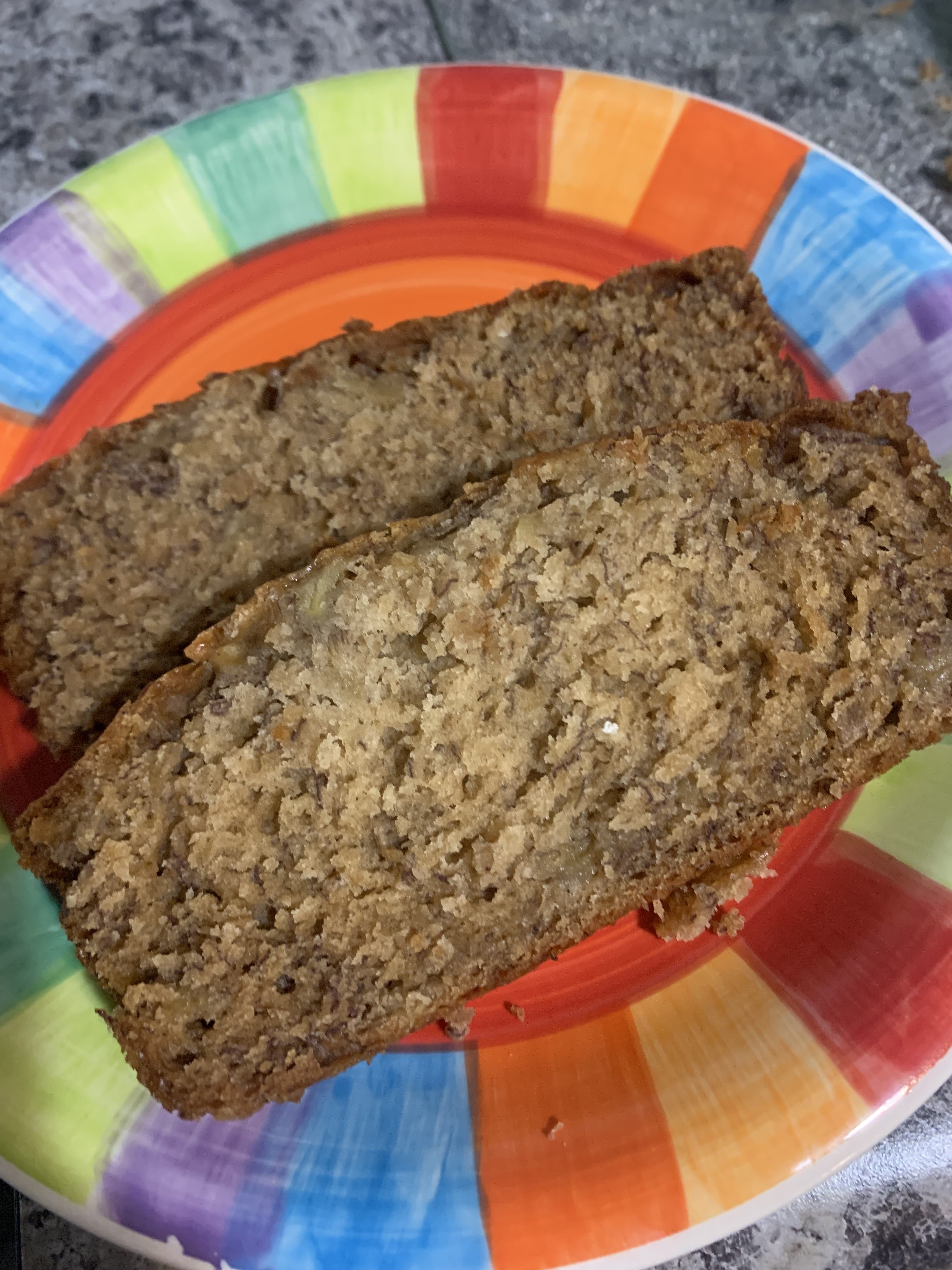 Two slices of banana bread on a colorful, rainbow-edged plate set on a gray countertop.
