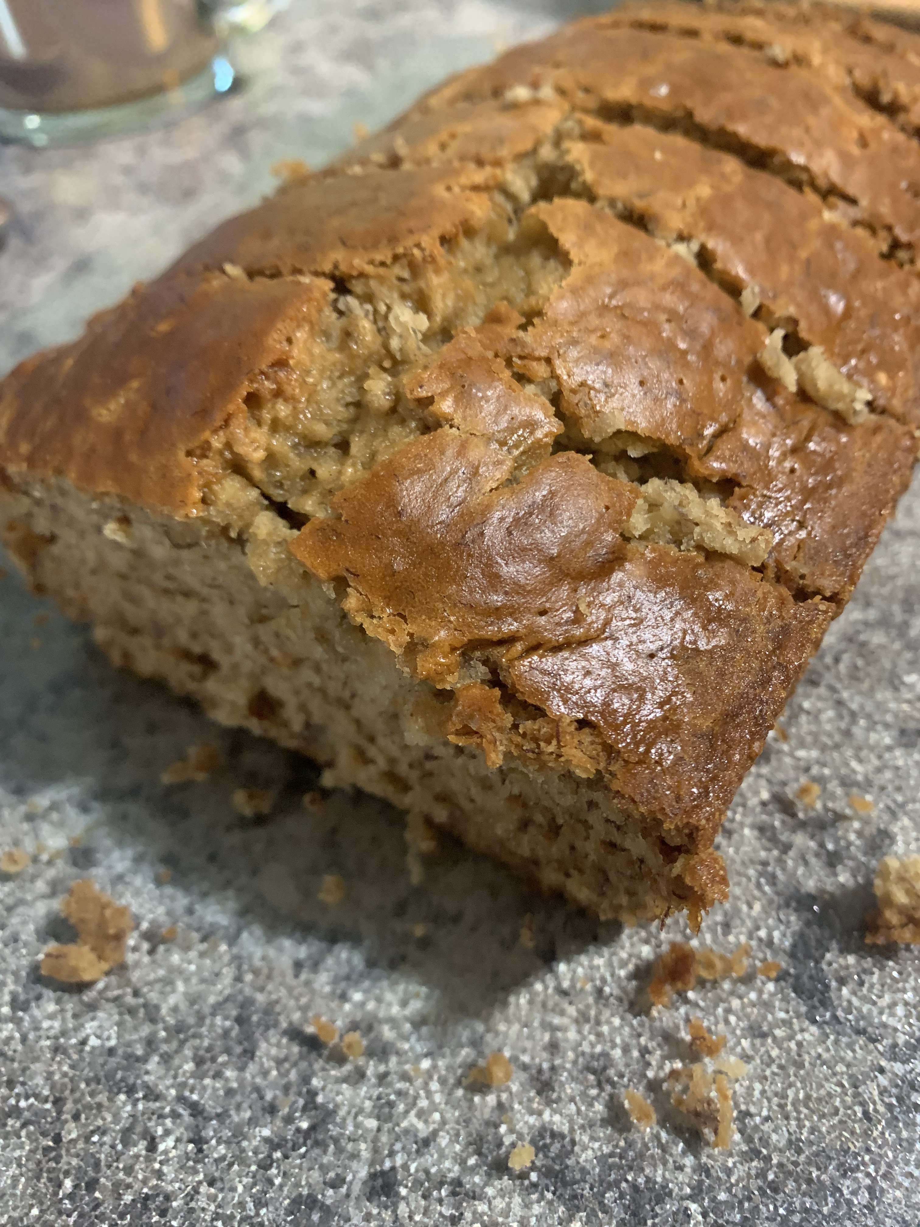 A close-up of a sliced loaf of banana bread on a countertop, with a golden-brown crust and crumbs nearby.