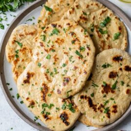 homemade naan on plate sprinkled with parsley.