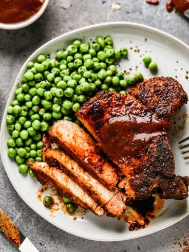 An air fryer pork chop on a plate with peas
