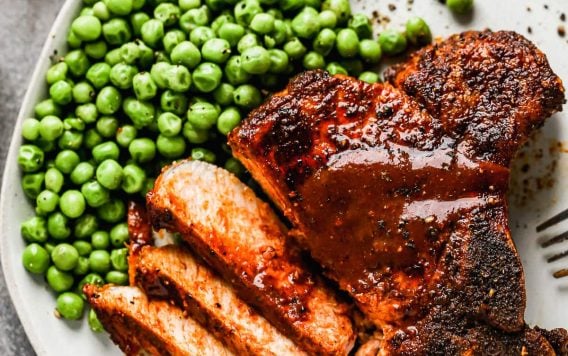 An air fryer pork chop on a plate with peas