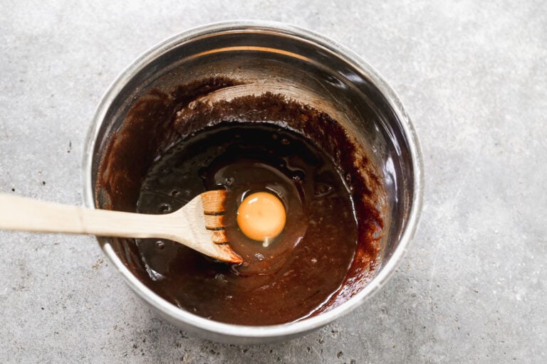 adding an egg to brownie batter in a metal bowl