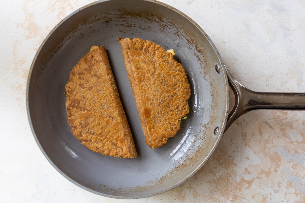 A skillet with 2 folded breakfast quesadillas, showing the browned tortilla sides.