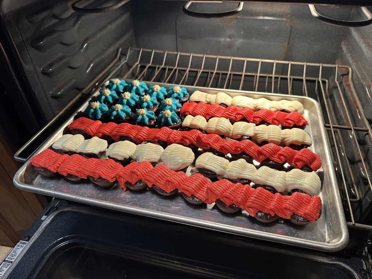 A tray of cupcakes decorated as a U.S. flag, with red, white, and blue icing, in an oven.