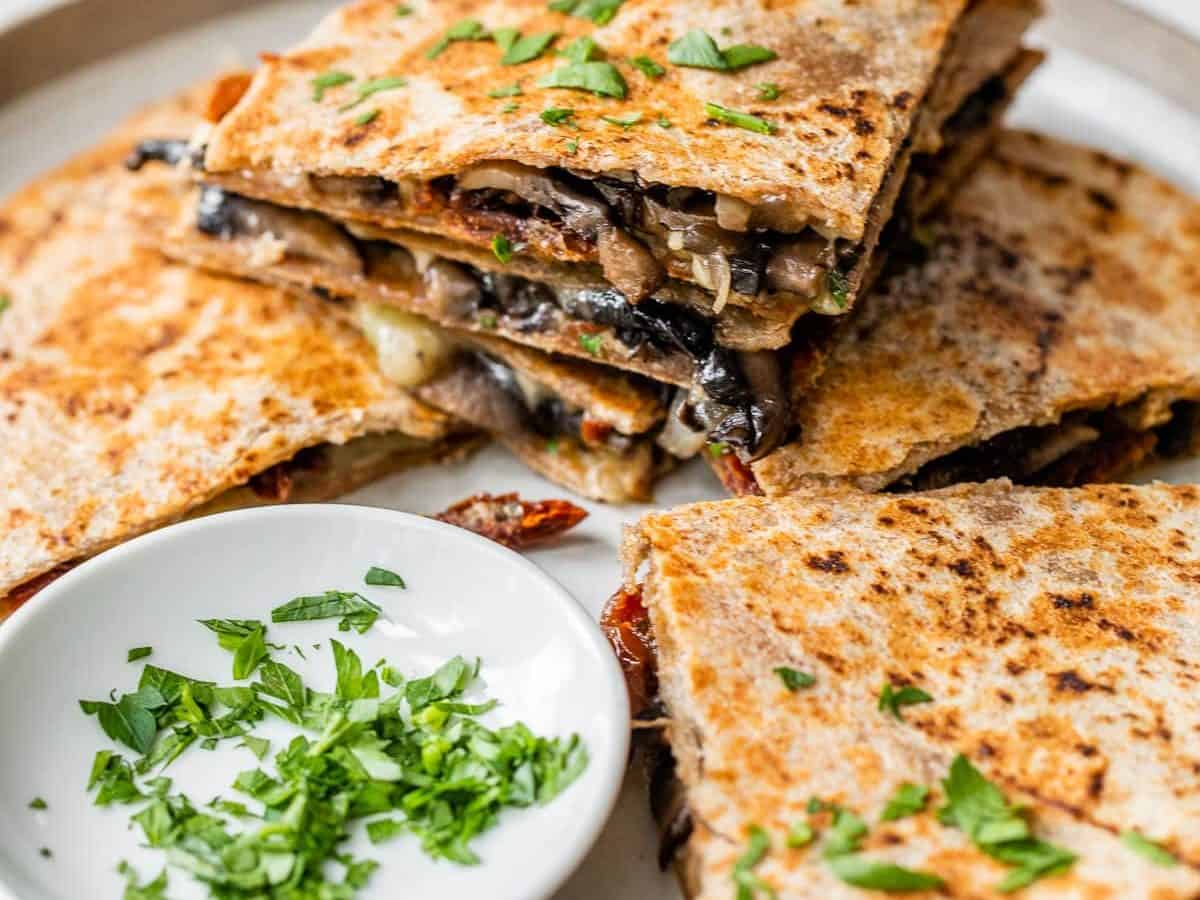 a cheesy mushroom quesadilla cut into wedges and stacked on a plate with herbs