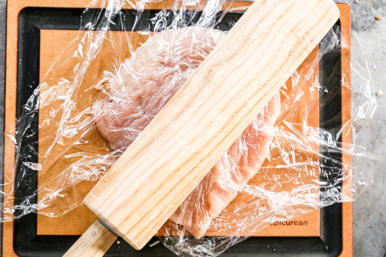 A chicken breast being flattened with a rolling pin