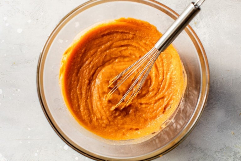 wet ingredients for pumpkin bread swirled with a whisk in a glass mixing bowl