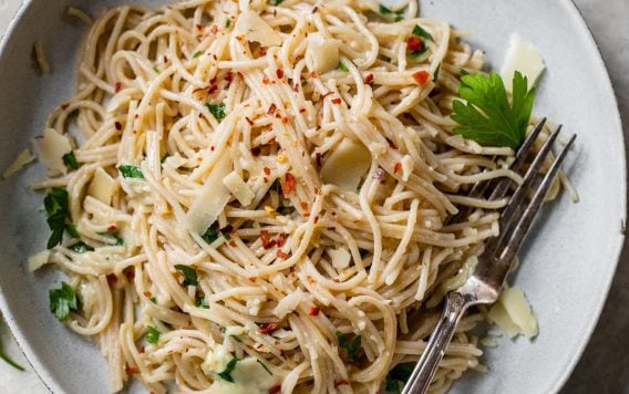 garlic pasta on a gray plate with a fork topped with parmesan