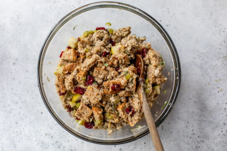 a mixture of bread cubes, apples, sausage, and cranberries in a glass bowl for stuffing muffins