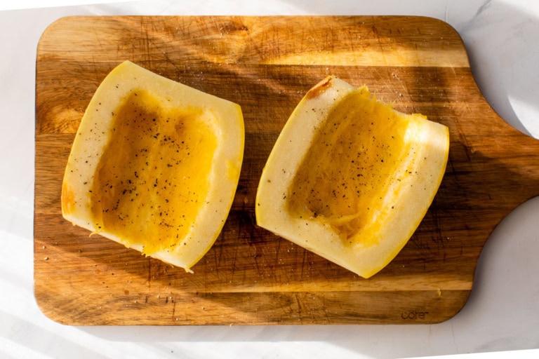 Two spaghetti squash halves on cutting board with insides scooped