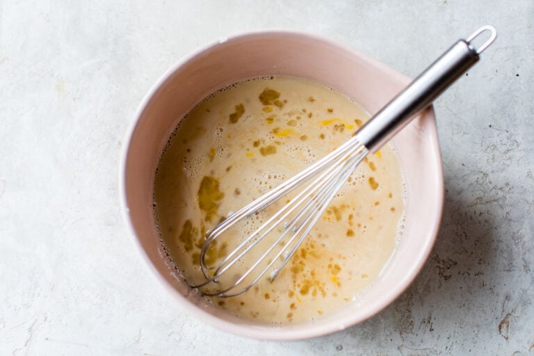 milk, maple syrup, and eggs in a mixing bowl with a whisk