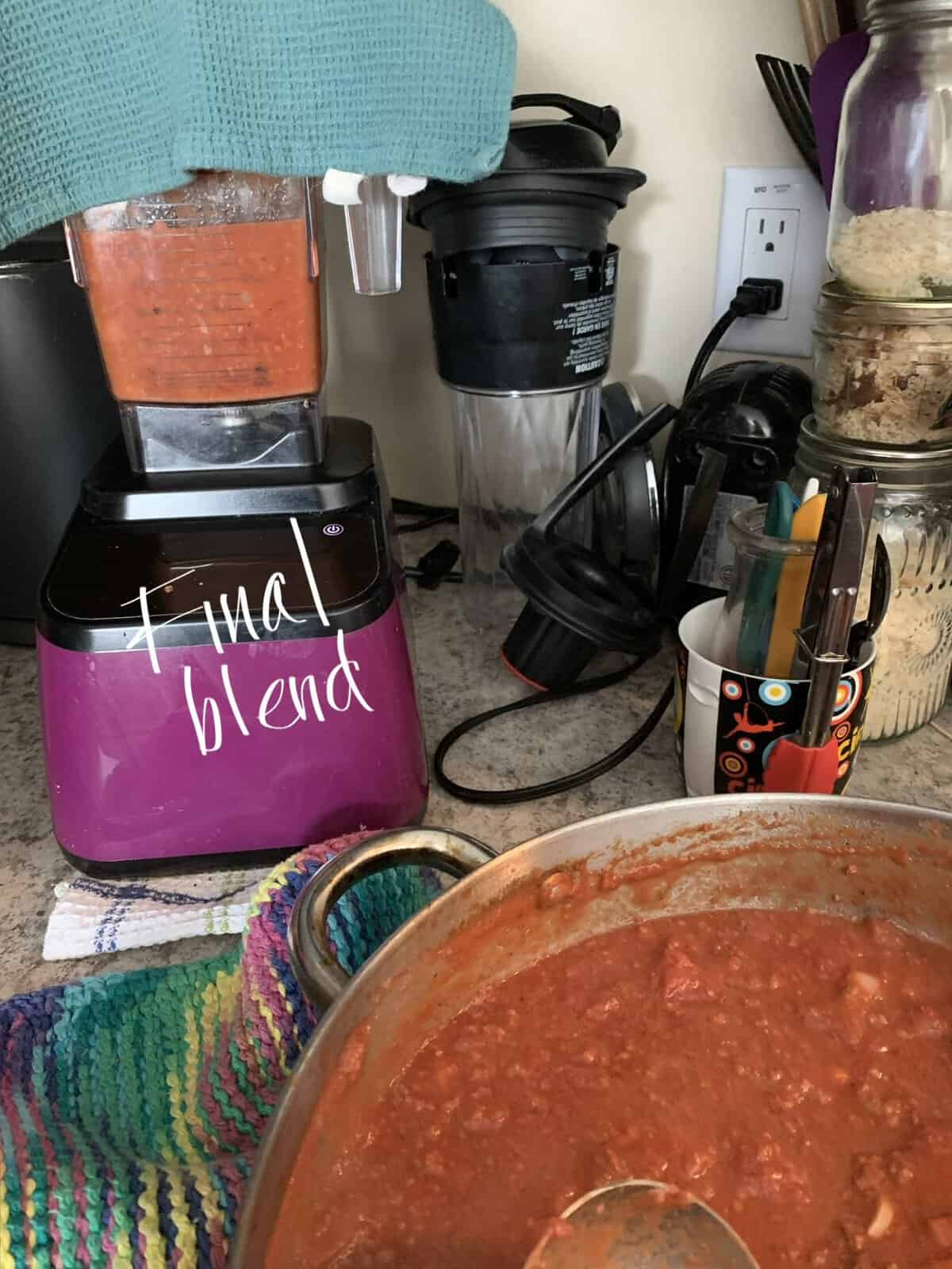 A blender labeled "final blend" mixes red sauce on a kitchen counter next to a pot of sauce, utensils, and colorful towels.