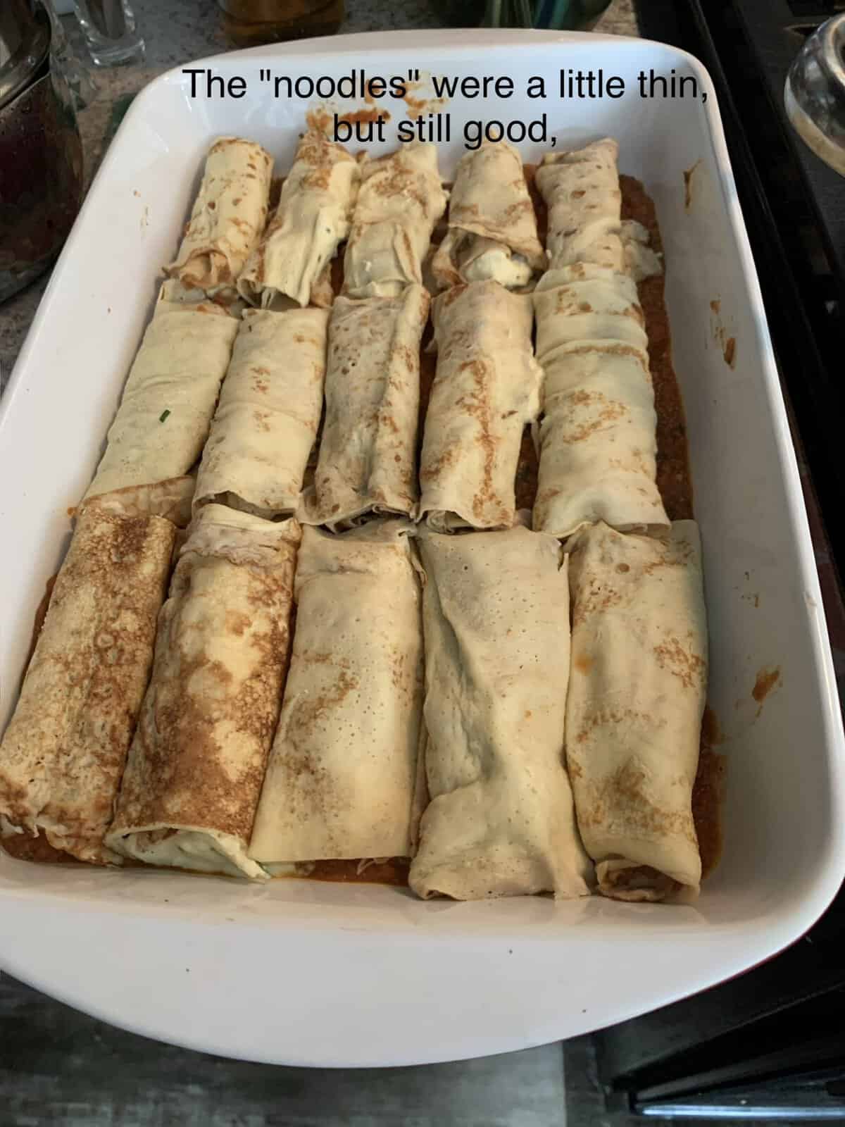 A casserole dish filled with rolled stuffed crepes used as noodles, on top of sauce, with text: "The 'noodles' were a little thin, but still good,.