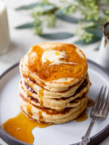 A stack of fluffy pancakes with butter and maple syrup