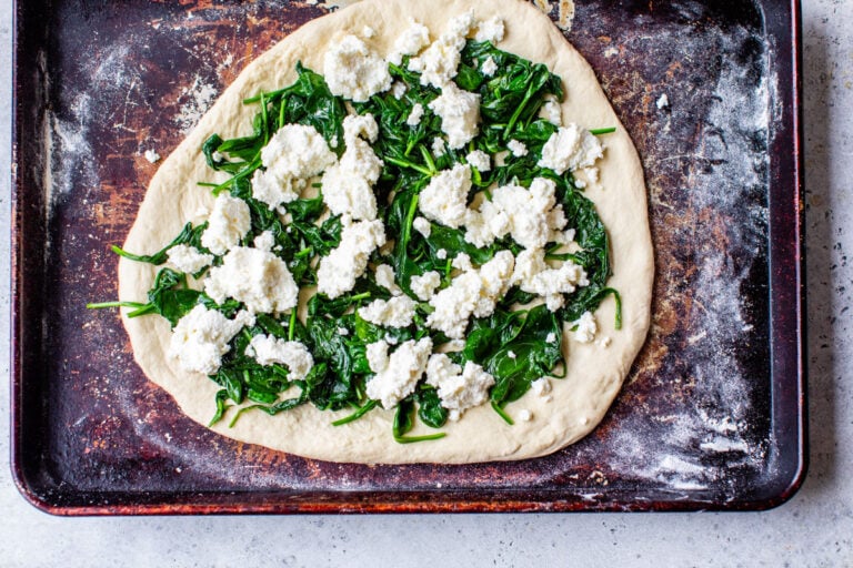 a homemade pizza topped with spinach and ricotta ready to be baked in the oven