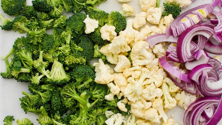 Chopped broccoli, cauliflower, and sliced red onions arranged on a white surface.
