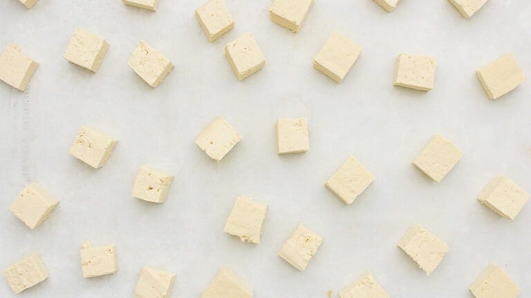 Small cubes of tofu are evenly spaced on a light-colored surface in a grid-like pattern.