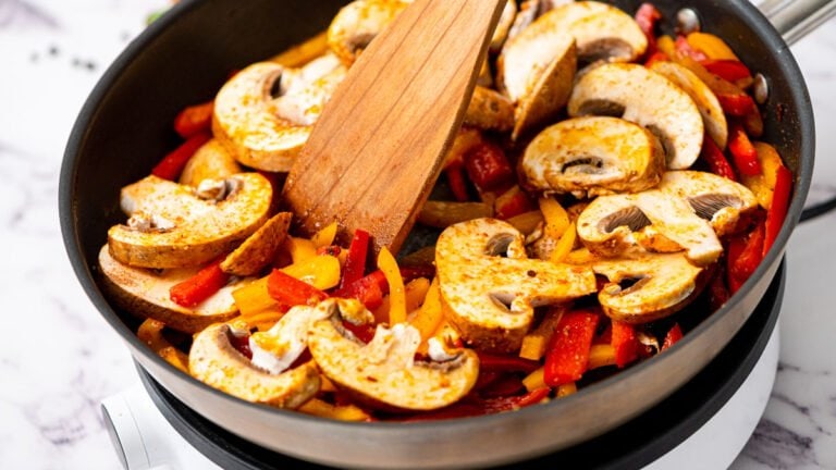 Mushrooms and peppers being stirred in a skillet